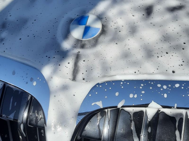 Espuma da pré-lavagem escorrendo pela grade de uma BMW durante a lavagem técnica